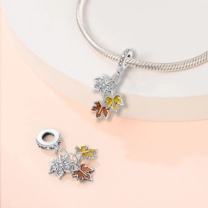 Detailed view of silver maple leaf charms with orange enamel and embedded crystals