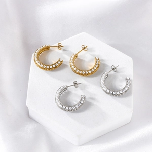 Detailed view of gold and silver C-shaped pearl earrings on a white marble stand