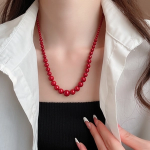 Détail d'un collier de perles rouges dégradées porté sur un pull noir minimaliste