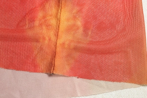 Detail von orange-rotem Mesh-Gewebe mit Fokus auf die Nahtverarbeitung und Versäuberung
