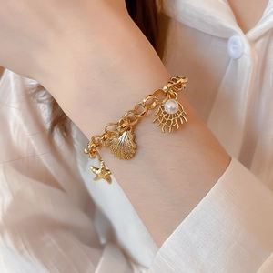 Detailed shot of gold starfish and shell charms with pearls on a seaside bracelet