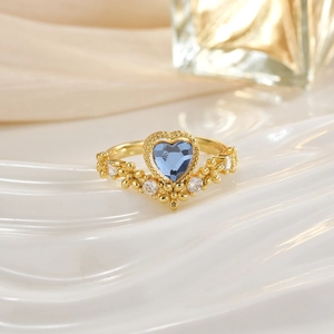 Close-up of golden crown ring featuring a blue heart gemstone with crystal accents