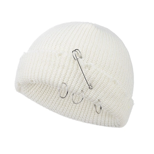 Detailed close-up of white knitted beanie featuring silver safety pin and metal rings accents