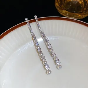 Boucles d'oreilles pendantes argentées avec zircon et perles sur plat blanc