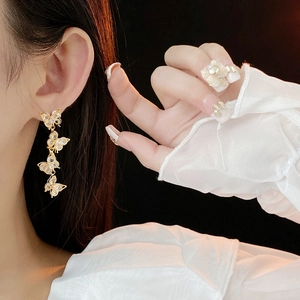 Close-up of golden butterfly tassel earrings with zircons worn on a model against black