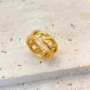 Macro detail of golden Cuban link ring with woven interlocking pattern on stone surface