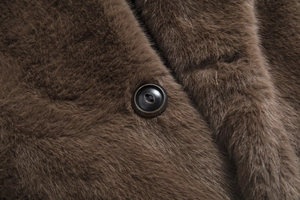Macro shot of brown faux fur texture and dark resin button detail on a winter coat