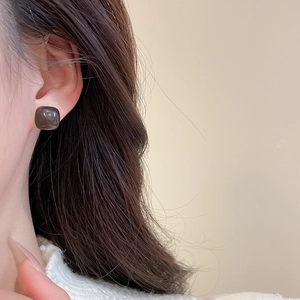 Close-up of a square resin stud earring in dark brown on a model's ear lobe