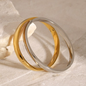 Minimalist gold and silver stainless steel bangles displayed on a natural stone base