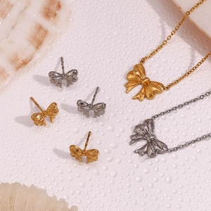Detail of 18K gold and silver bow pendant necklace and earrings on a shell background