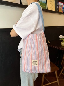 Grand sac cabas en maille rayée rose et bleu porté par un mannequin dans un café