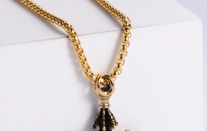 Detail of a gold box chain with a black enamel cross pendant on a white geometric block