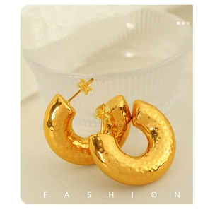 Detailed view of gold plated irregular hammer texture hoop earrings on white surface