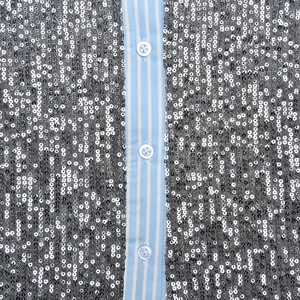 Detail of silver sequins and blue white striped fabric with white buttons on blouse