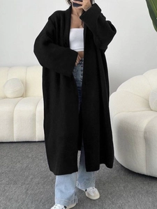 Long cardigan noir en maille pour femme avec haut blanc et jean dans une pièce moderne