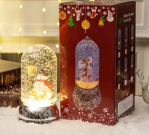 Close-up of lighted Christmas snow globe featuring a snowman and its festive gift box