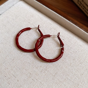 Macro shot of red wavy texture hoop earrings on a beige textured display tray