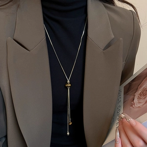 Close-up of golden tassel necklace with tiger eye bead on model in brown blazer