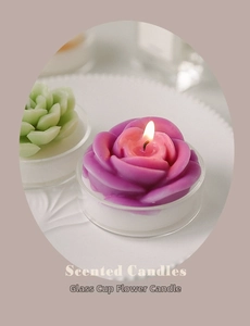 Detail of a lit purple rose and green succulent handmade scented candle in glass cup