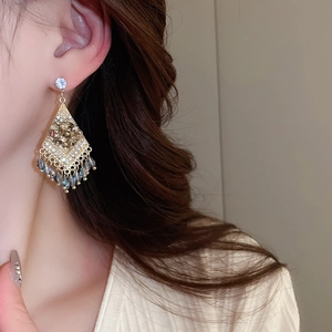 Close-up of diamond-studded rhombic tassel earrings with blue beads on a model