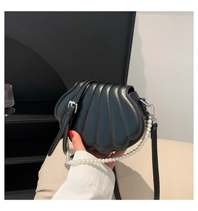 Detail of shell-shaped crossbody bag featuring faux pearl handle and glossy black texture