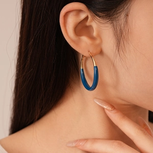 Detail of a minimalist gold and dark blue enamel hoop earring worn by a model