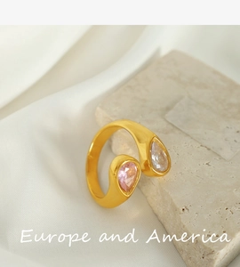 Close-up of gold open ring with clear and pink teardrop stones on white silk fabric