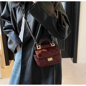 Detail of burgundy quilted leather texture with gold metal clasp on chain handbag