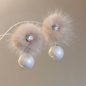 Detail of elegant gold plated earring with beige faux fur ball and white pearl texture