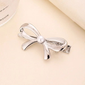 Elegant silver metal bow hair clip with white pearl centerpiece on a textured surface
