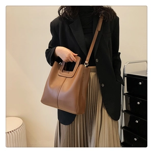 Brown leather bucket bag with top handle and adjustable strap shown on model in studio