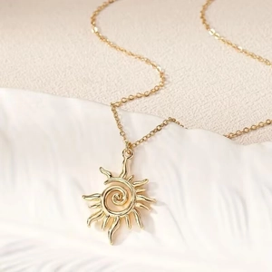 Close-up of golden sun swirl pendant with textured rays and fine cross chain necklace