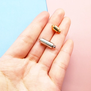 Detailed view of gold and silver magnetic jewelry clasps held in hand for scale