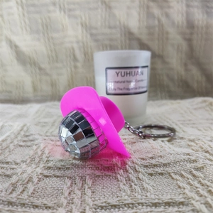 Detail of pink cowgirl hat and silver disco ball keychain on beige textured fabric
