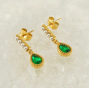 Macro shot of gold teardrop earrings featuring white pearls and green gemstones