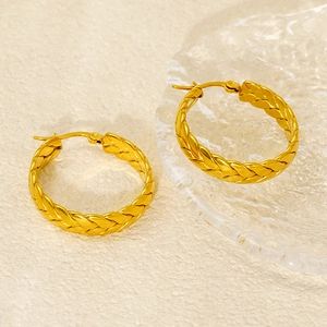 Detailed view of gold wheat-ear textured hoop earrings on a textured beige surface