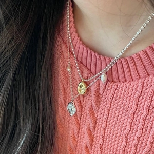 Detail of layered necklace featuring gold and silver pendants with elegant pearl accents