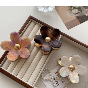 Three acetate flower hair clips in marble, tortoise, and white pearl finishes on a velvet tray