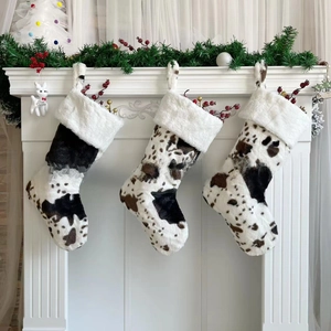 Three plush cow print Christmas stockings hanging on white fireplace mantle with holiday decor