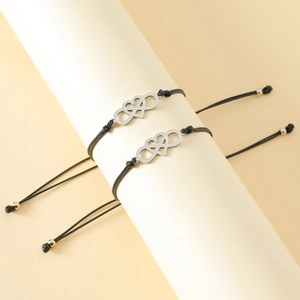 Detail of two black woven bracelets with silver infinity heart charms on a white stand