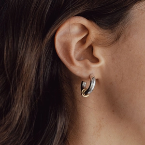 Close-up of a model wearing two-tone chunky hoop earrings in silver and 18k gold