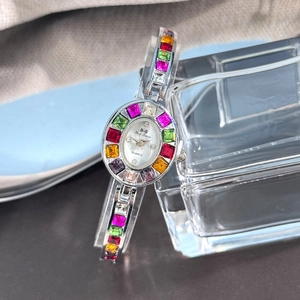 Detailed macro view of an oval quartz watch with colorful gemstones on a glass stand