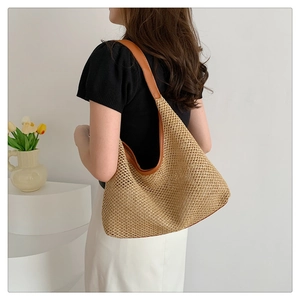 Close-up of straw tote bag with brown leather straps worn by a model in a minimalist room