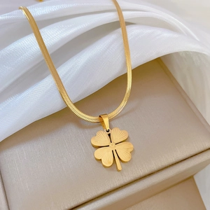 Detailed close-up of golden clover pendant on a flat snake chain over white silk fabric