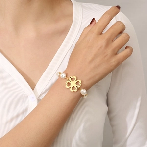 Gold plated four-leaf clover bracelet with hollow heart charms and white pearls on wrist