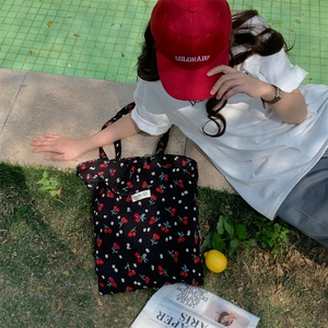 Close-up of black floral tote bag with cherry prints on lawn by a pool setting