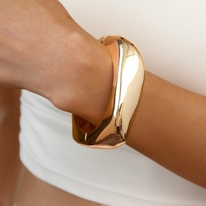Dettaglio di un ampio bracciale rigido dorato irregolare con finitura a specchio su modella