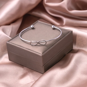 Silver infinity knot open cuff bracelet on elegant satin background with brown jewelry box