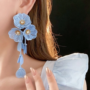 Détail de boucles d'oreilles fleurs bleu clair avec zircons et franges de pétales