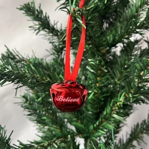 Red Christmas bell with Believe engraving and silk ribbon hanging on a tree branch